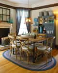 Dining room with wooden table, six chairs, pendant light, blue cabinet, and decorative bottles on a braided rug.