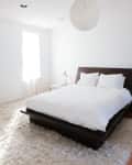 Minimalist bedroom with a dark wood bed frame, white bedding, fluffy rug, and a spherical ceiling light.