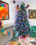 Colorful living room with a decorated Christmas tree, green sofa, vibrant artwork, and a sunburst mirror on the wall.