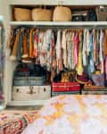 Open closet with colorful clothes, hats, and suitcases; floral bedspread in foreground.
