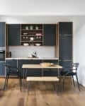 Modern kitchen with dark cabinets, wooden dining table, black chairs, and a framed artwork on a white wall.