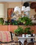 Eclectic living room with plants, abstract art, woven decor, and a rope chandelier over a white table.