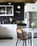 Modern kitchen with white cabinets, black tile backsplash, stainless steel appliances, and a round table with chairs.