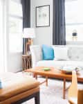 Bright living room with a gray tufted sofa, colorful cushions, wooden coffee table, and a leather chair by large windows.