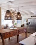 A rustic apothecary table used as a kitchen island in a white kitchen with natural fiber light shades