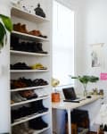 Home office with a desk, laptop, potted plant, shoe rack, and clothes hanging on a wall-mounted rack.