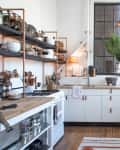 Industrial-style kitchen with open shelving, white cabinets, large plant, and washing machine.