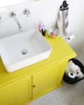 Yellow bathroom vanity with white sink, striped towel, toothbrushes, and rubber ducks on bathtub ledge.