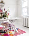 Dining room with white table, floral centerpiece, white chairs with striped cushions, colorful rug, and crystal chandelier.
