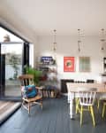 Dining room with wooden table, mismatched chairs, wall art, and open glass door to patio with plants.