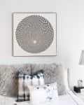 Bedroom with abstract art above bed, fluffy gray throw, tie-dye pillows, and silver pendant lamps.
