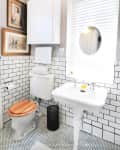 Small bathroom with white subway tiles, wooden toilet seat, pedestal sink, and framed art on the wall.