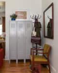 Gray lockers with a colorful framed print above, a coat rack with bags, and a yellow chair on wooden flooring.