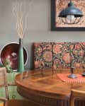 Dining area with patterned bench, round wooden table, decorative plates, and pendant light.