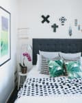 Bedroom with a gray headboard, tropical leaf pillows, orchid plant, and geometric wall decor.