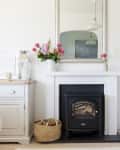 Living room with white fireplace, mirror, pink flowers, lanterns, and framed quote on wooden cabinets.
