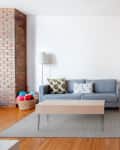 A clean, decluttered living space furnished with a three-seater blue sofa, coffee table, wooden desk, and a wooden dining table. A toy bin is located at a corner