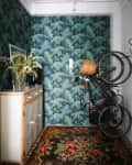Floral rug, tropical wallpaper, wooden cabinet with vase, and wall-mounted bicycle in a narrow hallway.