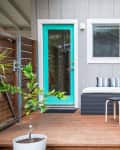 Patio with turquoise door, gray sectional sofa, striped cushions, small round table, and potted plant on wooden deck.