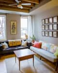 Cozy living room with a brown leather sofa, colorful cushions, a wooden coffee table, and framed botanical prints on the wall.