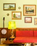 Retro living room with red sofa, green lamps, banjo, and framed landscape paintings on a light green wall.