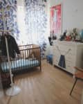 Nursery with wooden crib, blue leaf curtains, white dresser with toys, and a red poster on the wall.