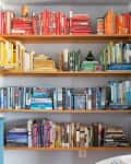 Color-coded bookshelf with red, yellow, green, blue, and black books, next to a blue dresser with a lamp and decor.