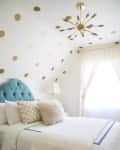 Bedroom with blue tufted headboard, gold polka dot wall, fluffy pillows, and modern chandelier.