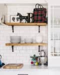 Kitchen with white cabinets, wooden shelves, blue kettle, mixer, and plaid bag on shelf.