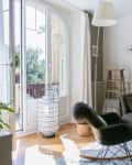Cozy living room with a gray sofa, patterned cushions, rocking chair, and large window with sheer curtains.