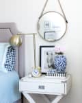 Bedroom nightstand with a gold lamp, round mirror, blue floral vase, books, and a framed horse photo.