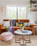 Cozy living room with orange sofa, colorful throws, round coffee table, and plants, creating a vibrant, inviting space.