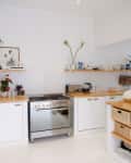 Modern kitchen with white cabinets, wooden countertops, stainless steel oven, and open shelves with plants and decor.