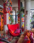 Eclectic living room with vibrant red chair, colorful pillows, hanging glass ornaments, and diverse wall art.