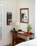Small home office with wooden desk, chair, potted plant, lamp, and Vogue poster on wall.