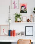 Home office with white desk, plants, books, framed art, and a dreamcatcher on the wall.