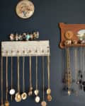 Necklaces and rings displayed on vintage wall hooks against a dark blue wall.