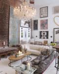 Loft-style living room with a crystal chandelier, brick wall, eclectic art, tufted sofas, and a wooden coffee table with candles.
