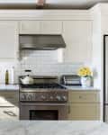 Modern kitchen with cream cabinets, stainless steel stove, marble countertops, yellow mixer, and potted plant by window.