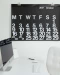 Minimalist office with a large black calendar for October 2017, white desk, iMac, and white chair.