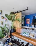 Living room with colorful masks on the wall, leather sofa, striped cushions, plants, and a blue accent wall with dining table.