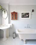 Elegant bathroom with a clawfoot tub, pedestal sink, ornate mirror, and wooden cabinet on tiled walls.