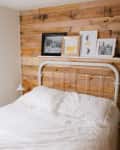 a bed with white bedding and wrought iron headboard sits against a pallet wood wall