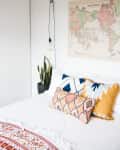 Bed with patterned pillows, a hanging bulb, a potted plant, and a vintage world map on the wall.