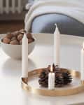 Candles in gold holders and a bowl of walnuts on a white table.
