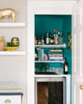 Shelves with decor items, including a red bust and gold pig, next to a teal bar nook with bottles and glassware.