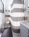 Small bathroom with gray and white striped shower curtain, white cabinet, round mirror, and gray rug.