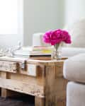 Rustic wooden coffee table with pink peonies in a jar, books, and a beige sofa in the background.