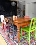 Dining room with wooden table, colorful chairs, patterned rug, and chalkboard wall.