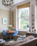 Living room with beige walls, blue chairs, round table, large artwork, chandelier, and a cat on the windowsill.
